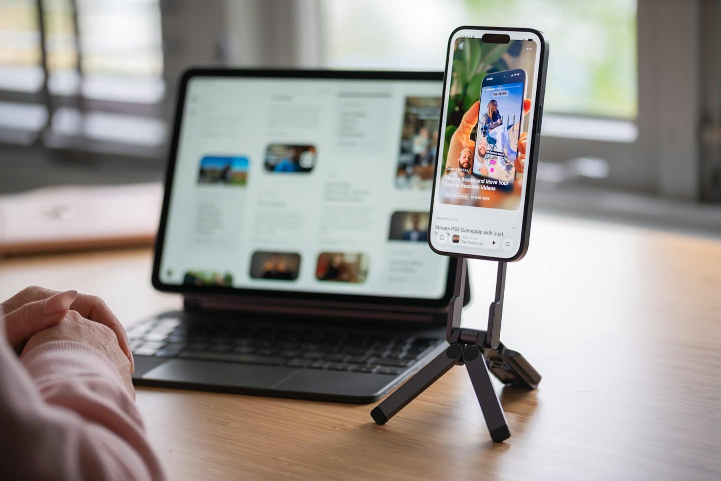 Hands rest on a wooden desk near a tablet and smartphone.