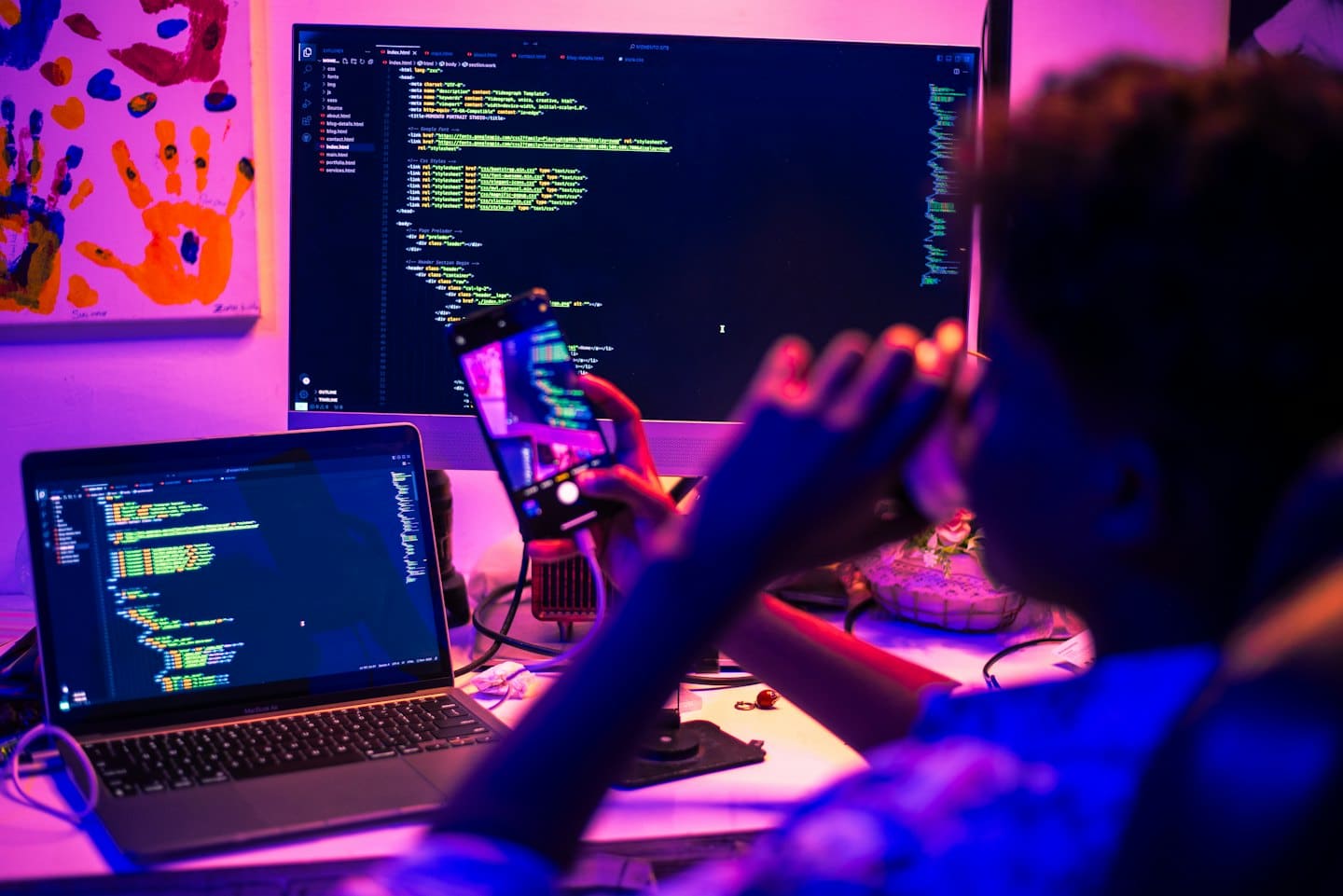 Software developer works with code on multiple screens and smartphone.